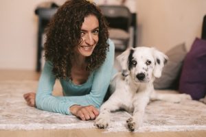 Una perrita blanca posa junto a su dueña sobre la alfombra